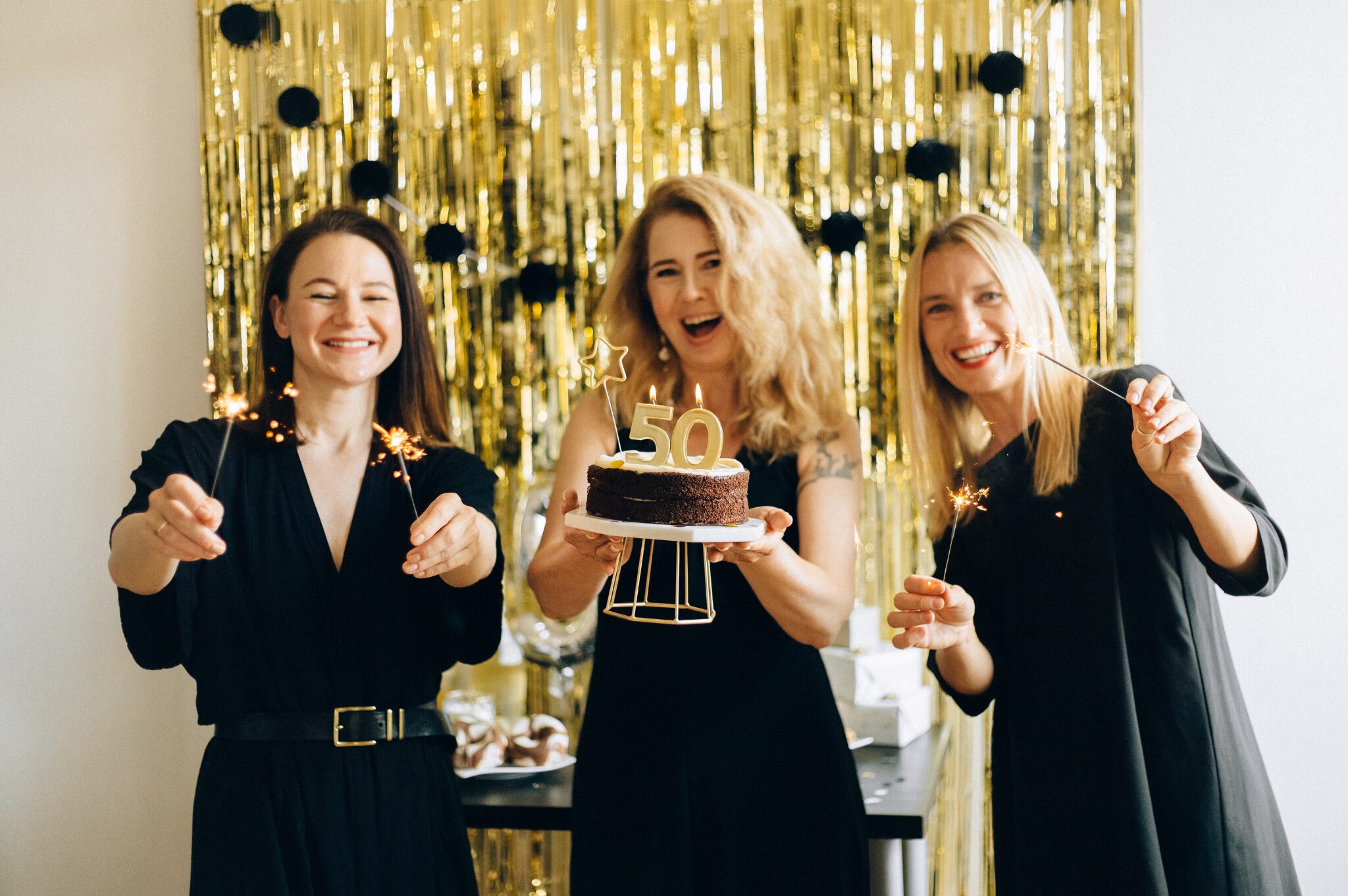 50thbirthdaywomen Group of women smiling and posing with a decorated cake celebrating a 50th birthday milestone.