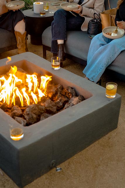 Team members relaxing around a modern outdoor firepit, enjoying drinks and dinner during a corporate retreat.