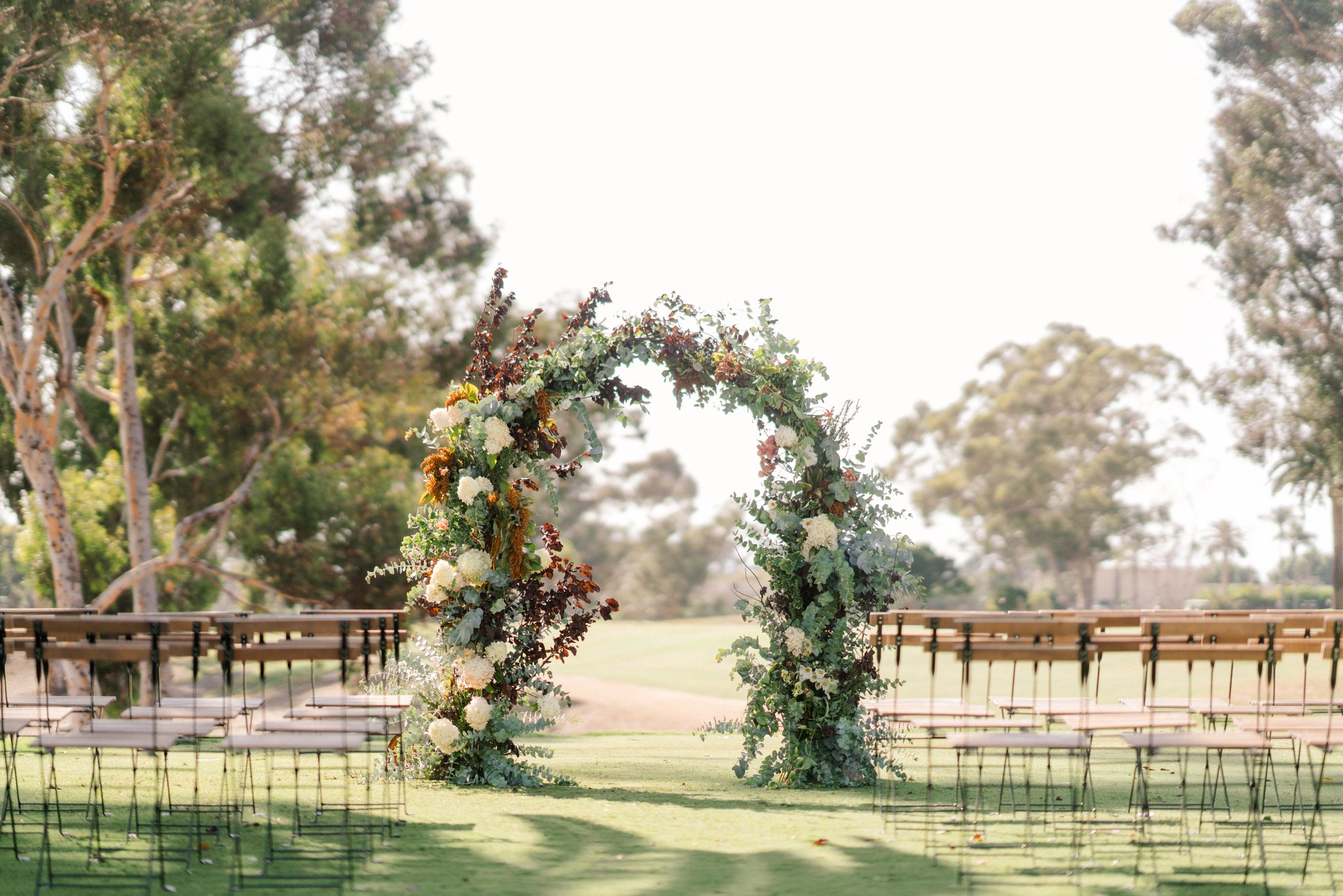 Sourced Shoot Luxury outdoor ceremony setup with circular floral arch, organic greenery, and elegant seating in an estate setting