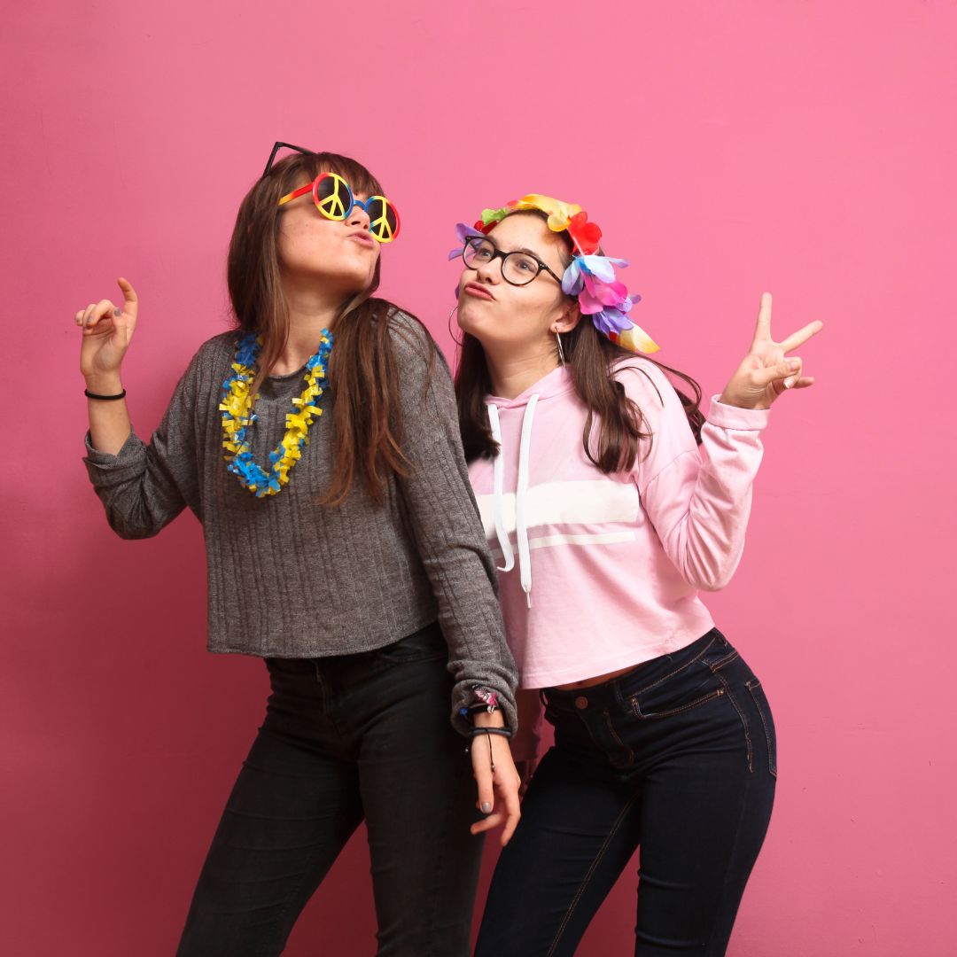 Two guests posing with fun photo booth props against a pink backdrop
